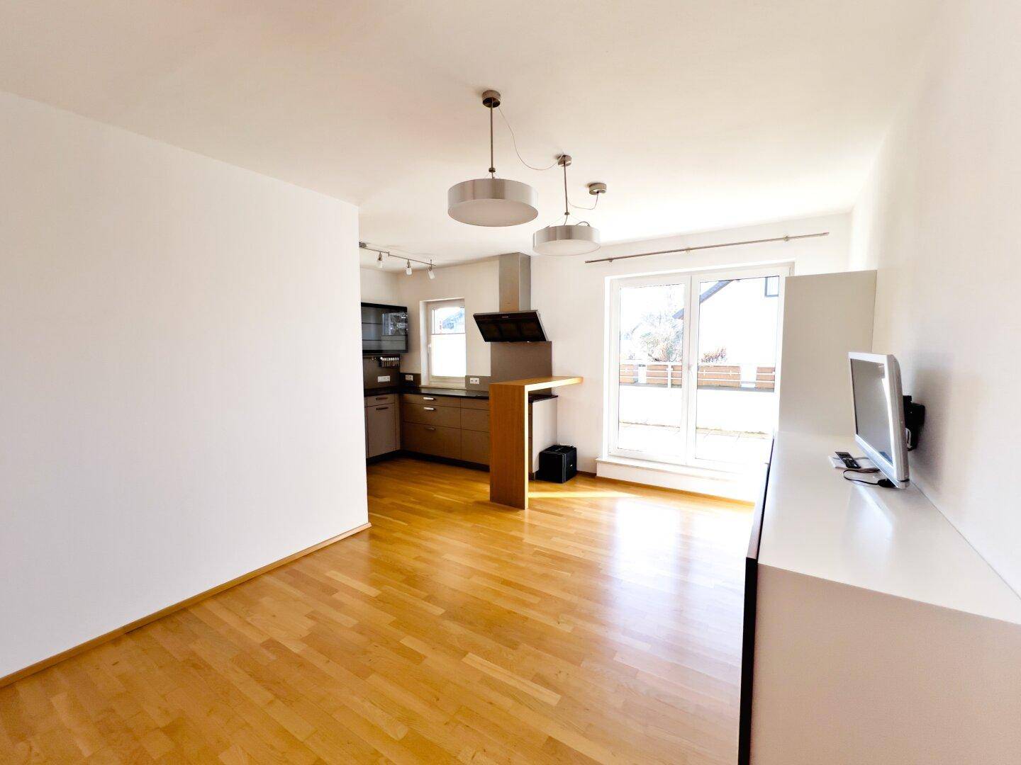 Offener Wohnbereich mit Holzboden und Übergang zu einer modernen Küche mit Bar.