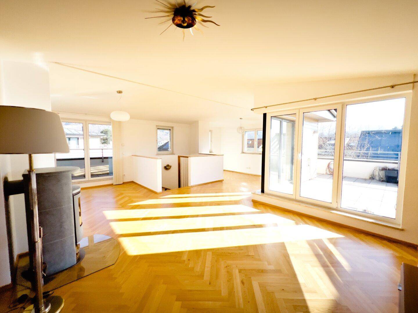 Helles Wohnzimmer mit Fischgrätparkett, Kaminofen und Zugang zu einer sonnigen Terrasse.