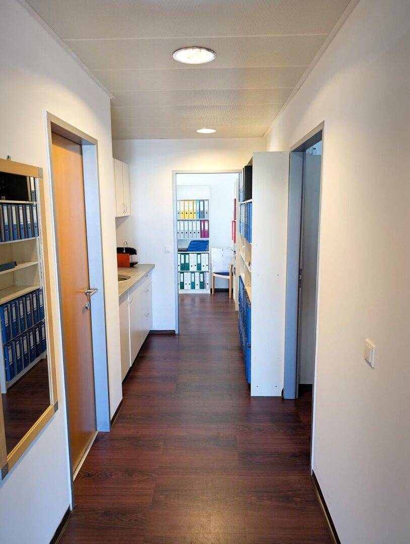 Langer Flur mit dunklem Holzboden, weißen Wänden, Regalen und einer integrierten Küchenzeile.