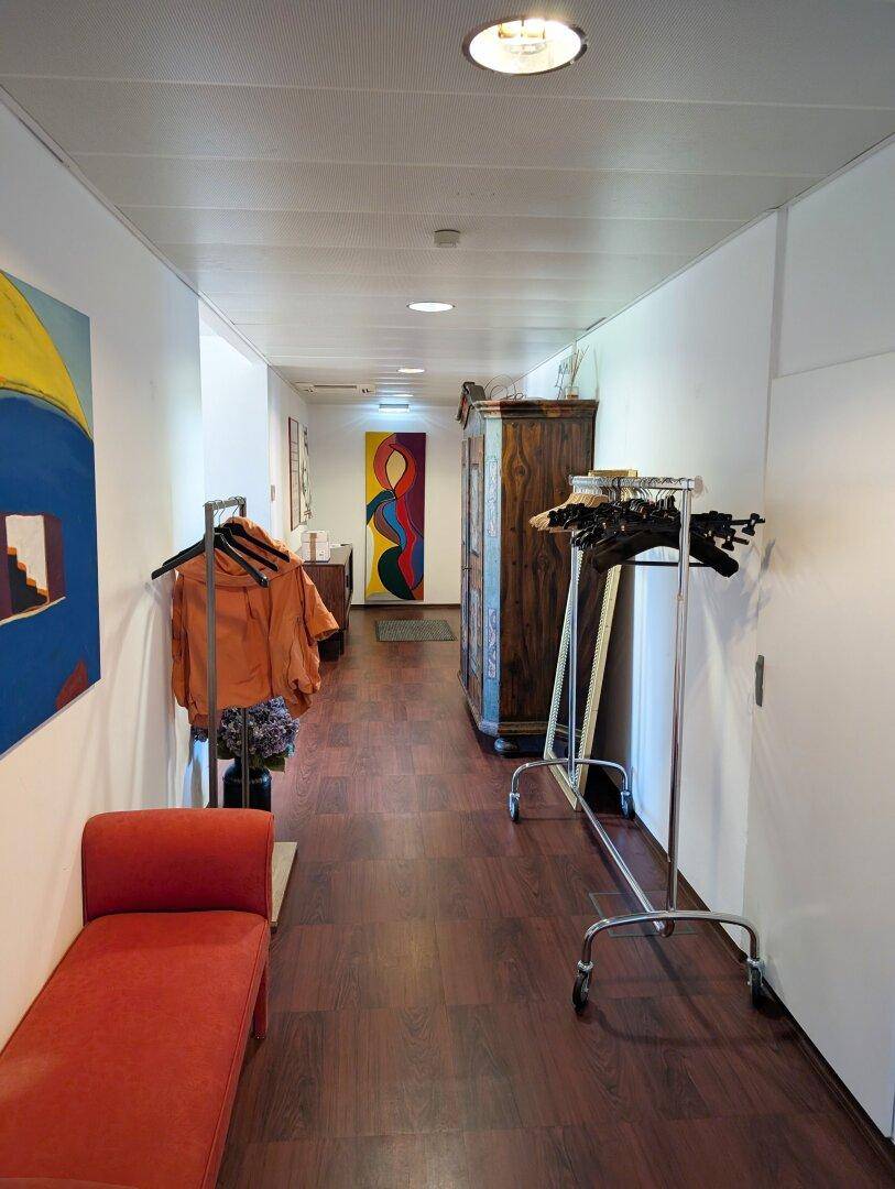 Geräumiger Flur mit Holzboden, farbenfrohen Kunstwerken, einem antiken Schrank und Kleiderständern.