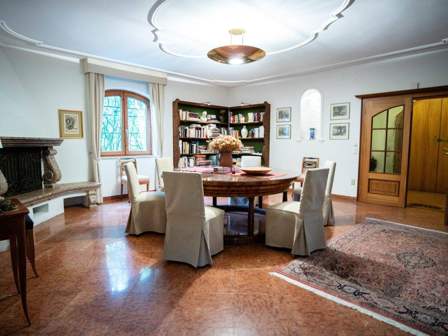 Klassisches Esszimmer mit rundem Holztisch, Marmorboden und dekorativer Deckenverzierung.