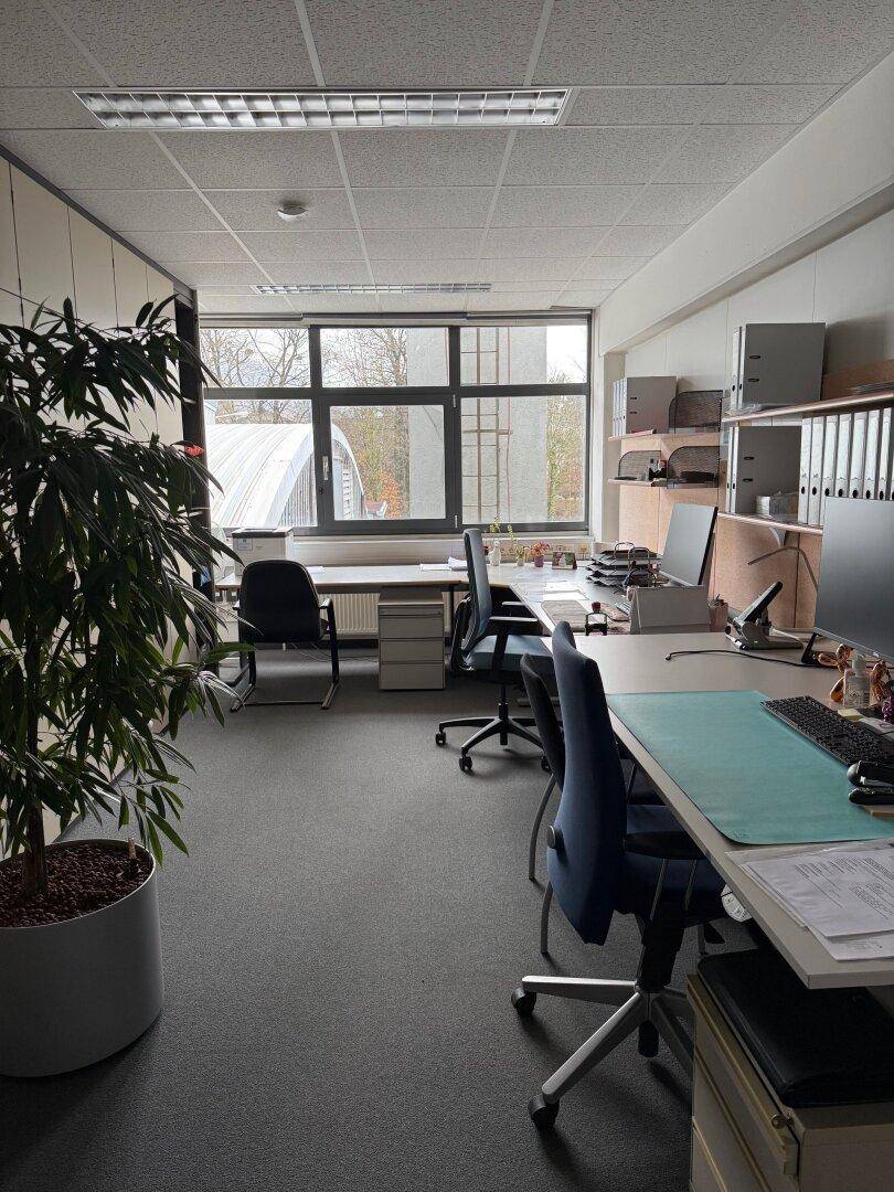 Helles Büro mit mehreren Arbeitsplätzen, Computern und einer großen Fensterfront mit Ausblick.