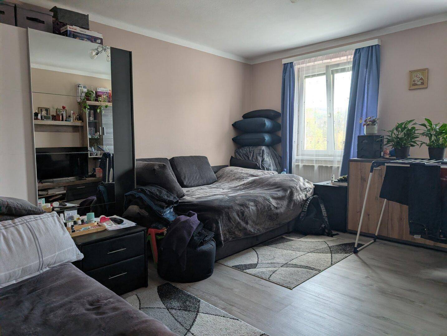 Gemütliches Schlafzimmer mit Bett, Schrank und Fenster, das viel Tageslicht hereinlässt.