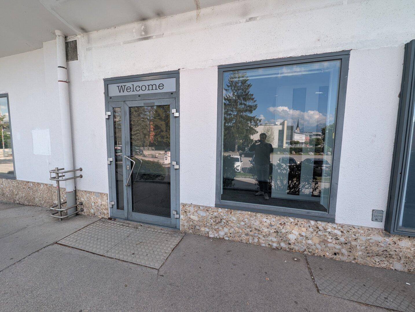 Gebäudeeingang mit einer barrierefreien Rampe und großen Schaufenstern.