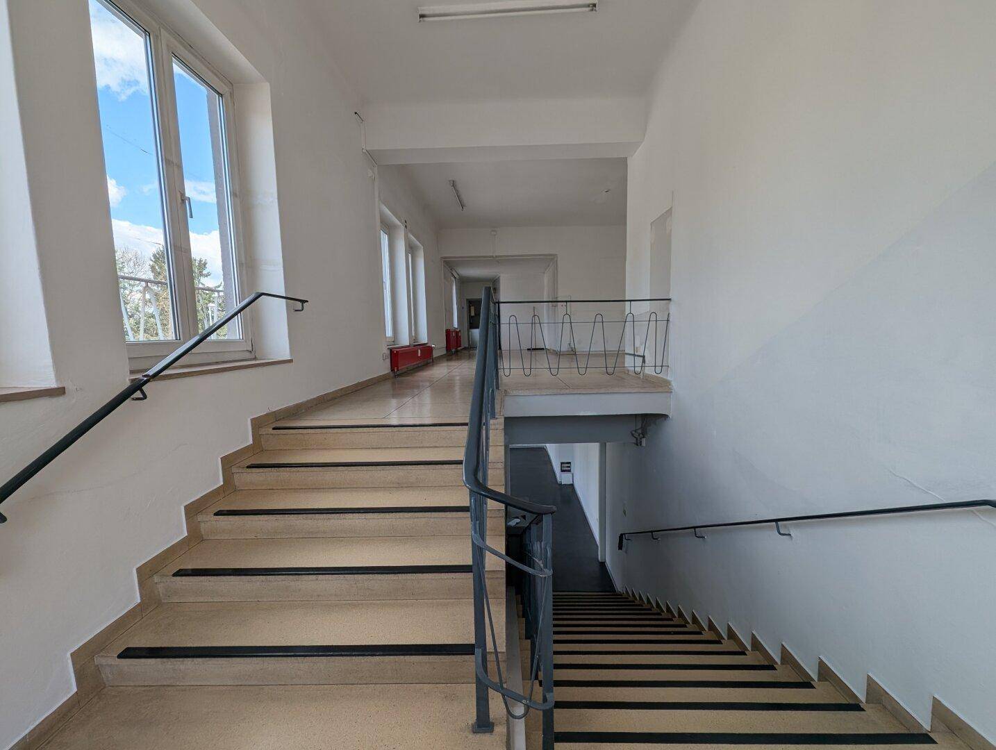 Helles Treppenhaus mit großen Fenstern, die viel Tageslicht hereinlassen, und stabilen Handläufen.