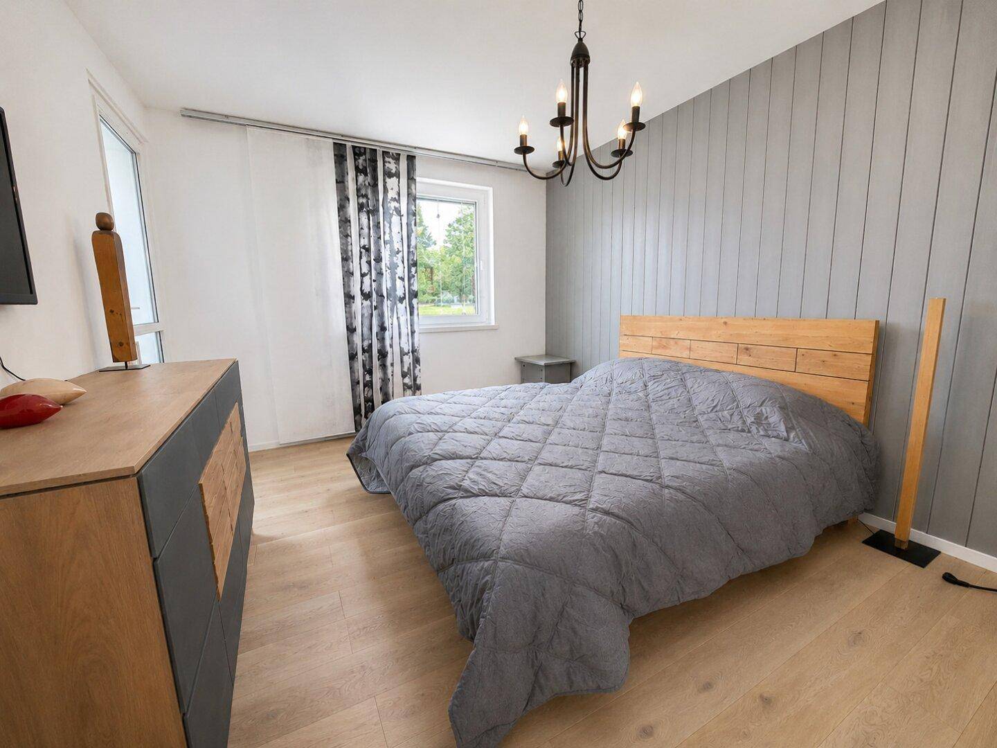 Helles Schlafzimmer mit Holzbett, grauer Akzentwand und hellem Laminatboden.