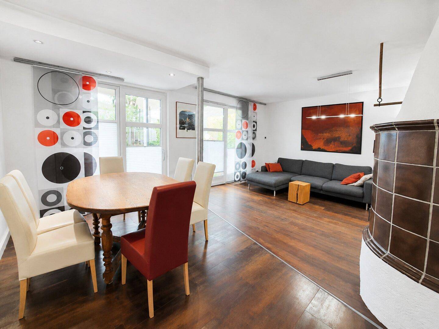 Geräumiger Wohn-Essbereich mit dunklem Holzboden, modernem Sofa und traditionellem Kachelofen.