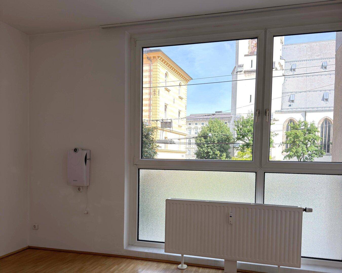 Leerer Raum mit großem Fenster, das einen Blick auf die Stadt und historische Gebäude bietet.