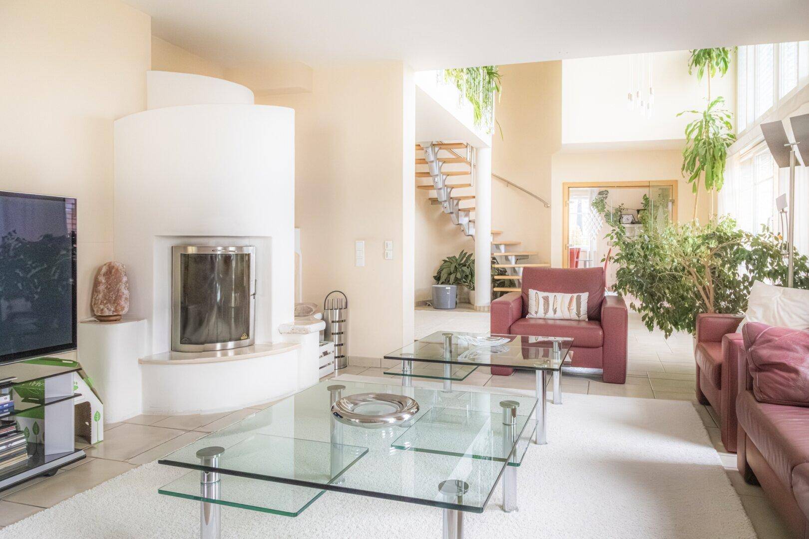 Helles Wohnzimmer mit modernem Kamin, bequemen Sofas und einer offenen Wendeltreppe im Hintergrund.