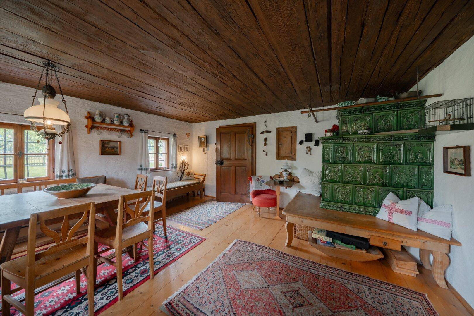 Gemütlicher Wohn-Essbereich mit traditionellem Kachelofen, Holzbalkendecke und rustikalen Holzmöbeln.