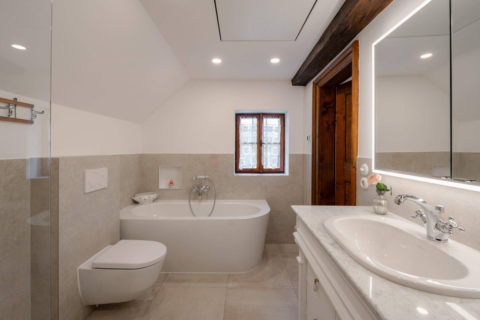 Modernes Badezimmer mit freistehender Badewanne, Wand-WC, Einzelwaschbecken und beleuchtetem Spiegelschrank.