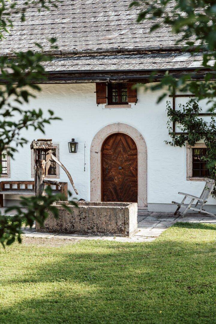Traditionelles Bauernhaus mit weißer Fassade, Holztür und einem alten Brunnen im Vorgarten.