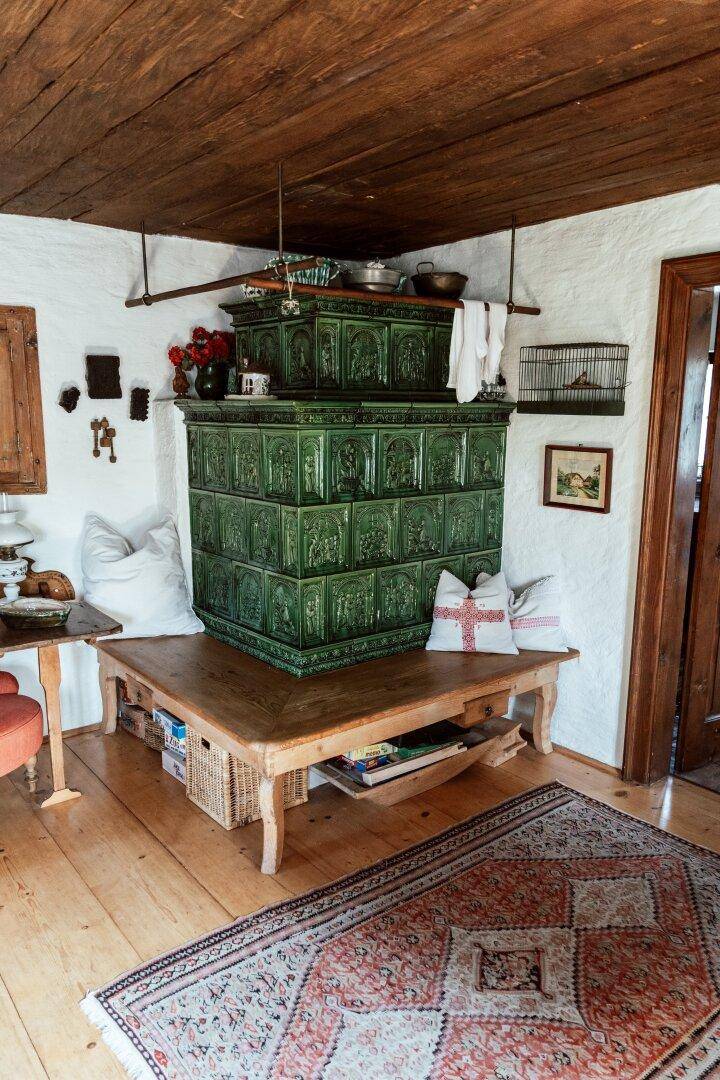 Traditioneller Wohnraum mit einem großen grünen Kachelofen und Holzbalkendecke.