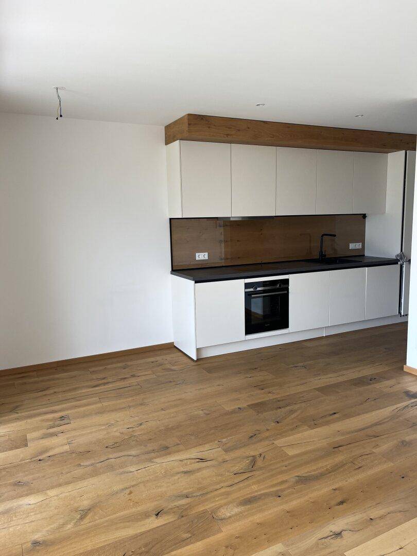 Moderne Einbauküche mit weißen Schränken, dunkler Arbeitsplatte und integriertem Backofen.