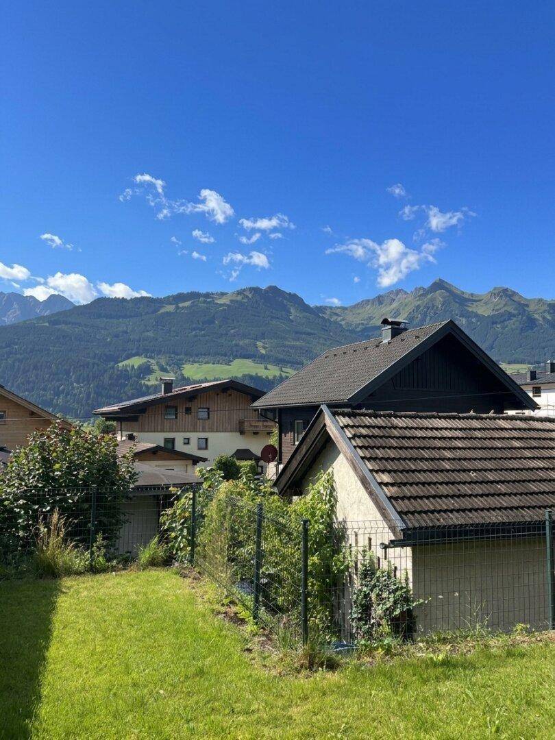 Grüner Gartenbereich mit Blick auf benachbarte Häuser und die umliegende Berglandschaft.