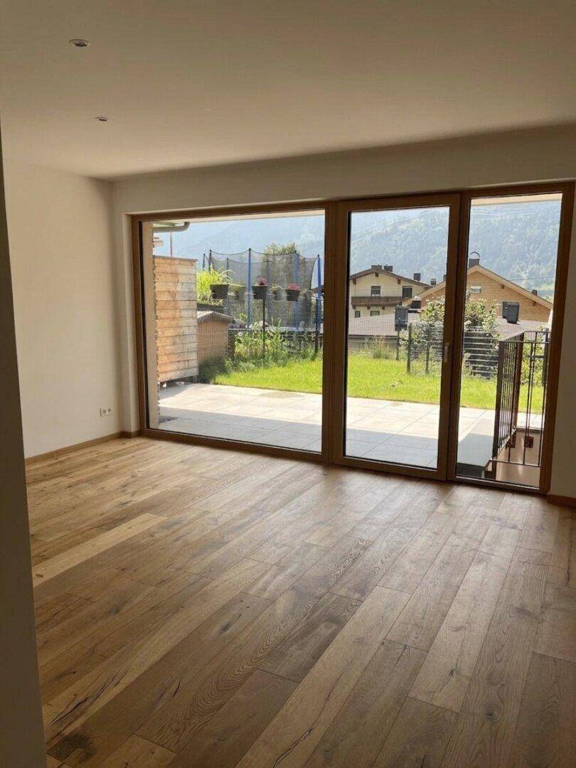 Heller Wohnraum mit Eichenparkett und großen Glasfronten zum Garten mit Bergblick.