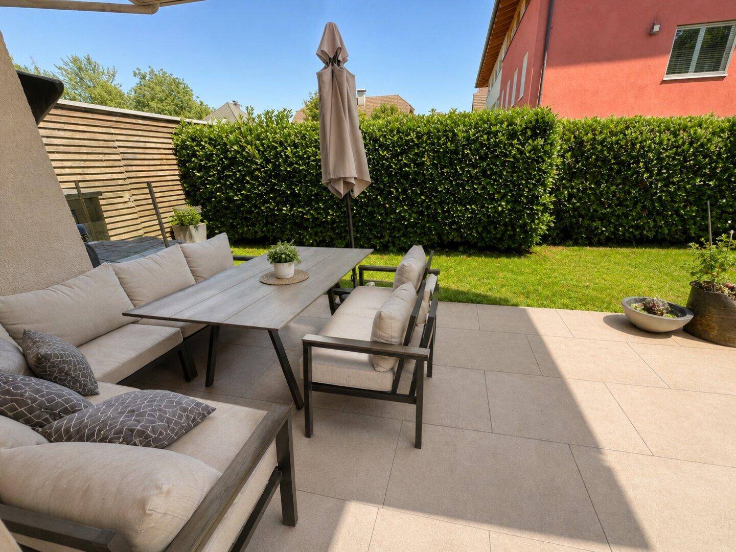 Große, sonnige Terrasse mit bequemen Gartenmöbeln und Blick auf den gepflegten Rasen.