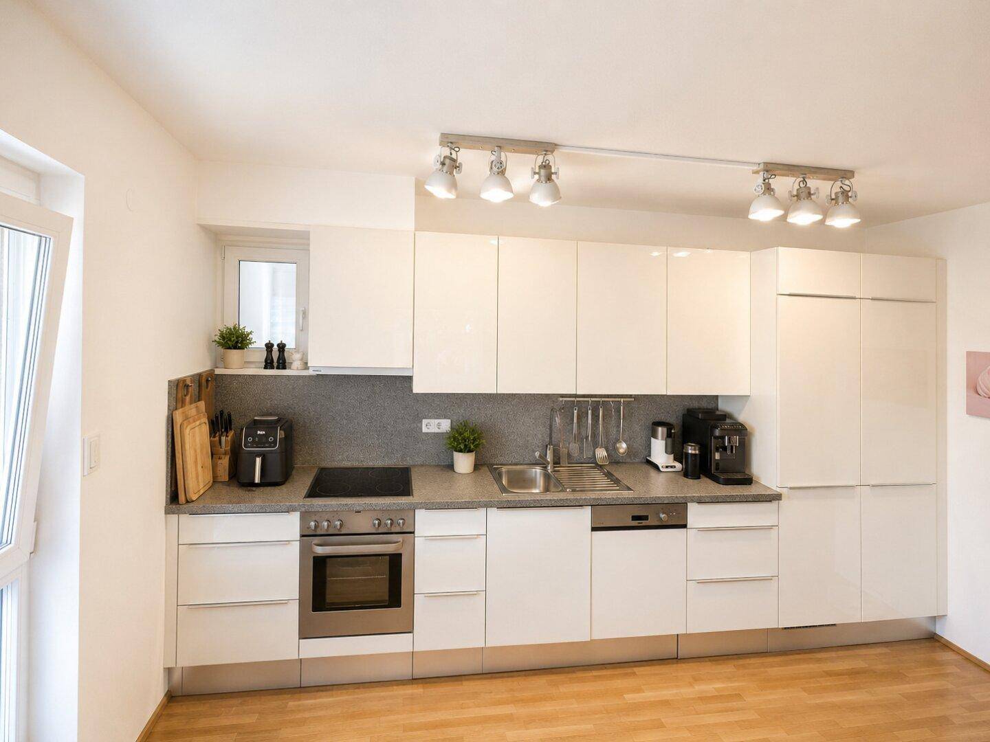 Moderne Einbauküche mit weißen Hochglanzfronten, integrierten Geräten und Holzparkettboden.