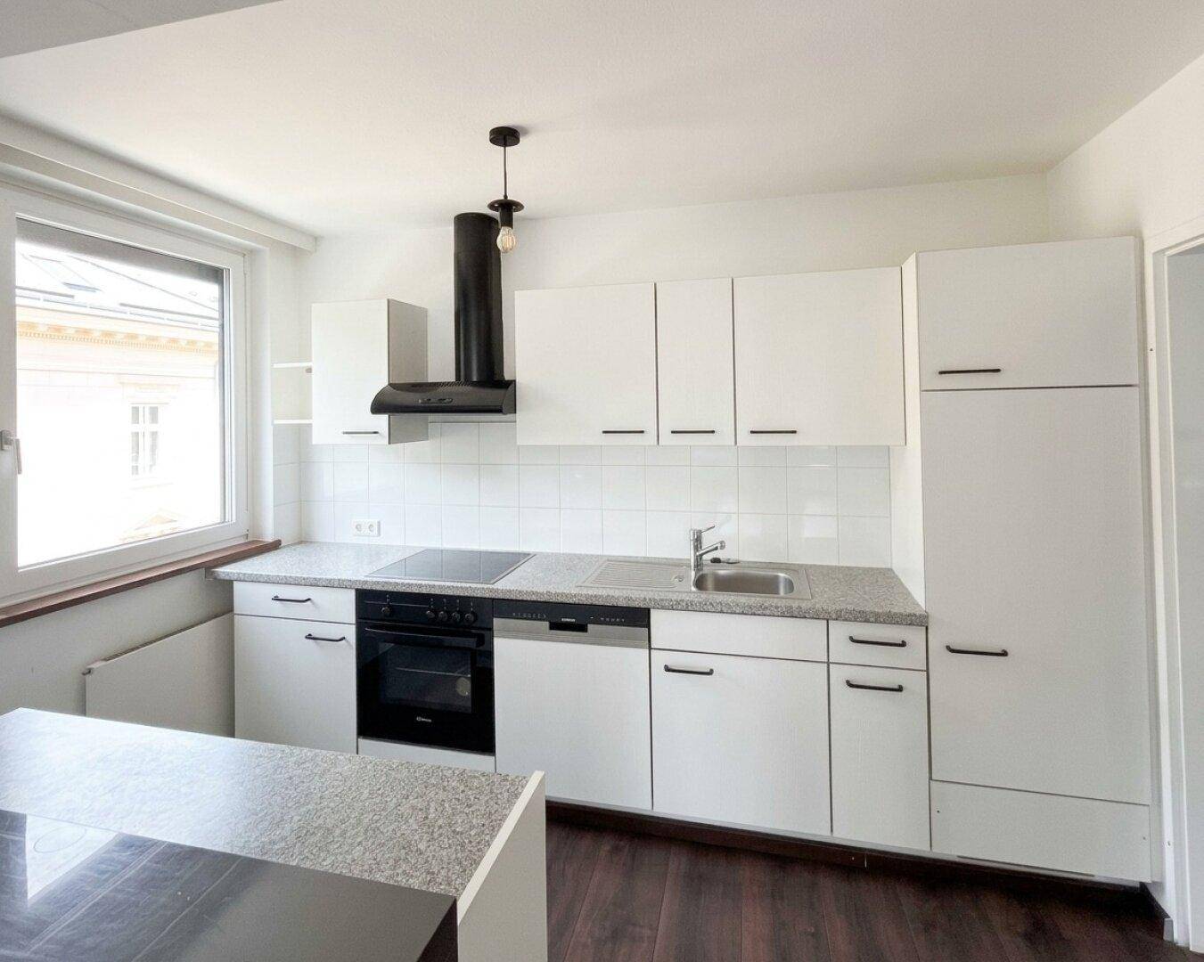 Moderne Einbauküche in Weiß mit Granitarbeitsplatte, Induktionskochfeld und Fenster.