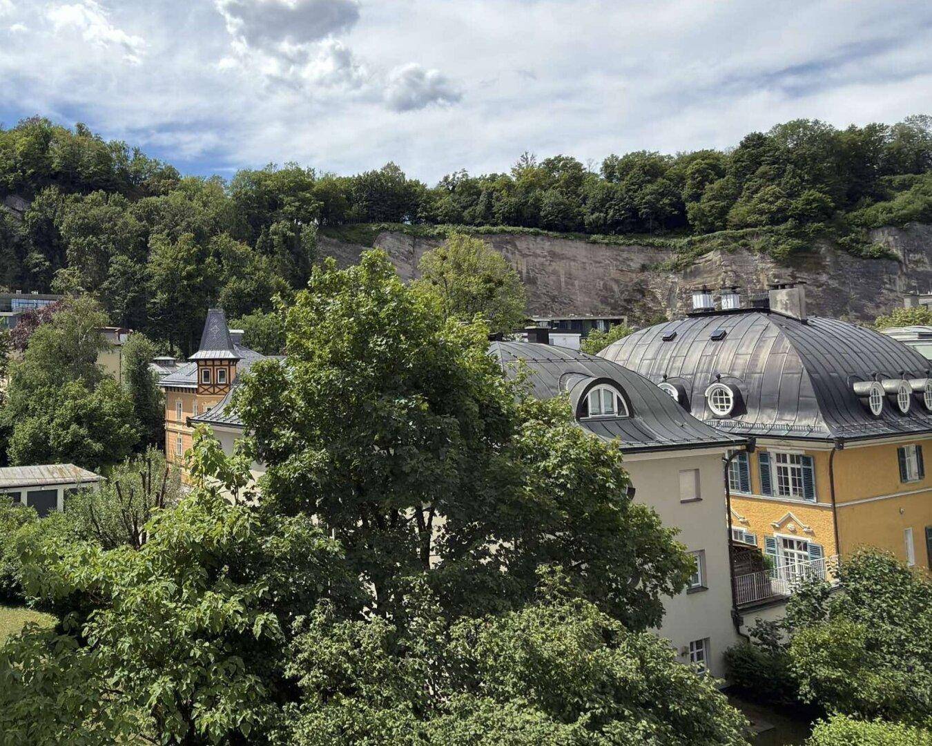 Panoramablick auf historische Gebäude, grüne Hügel und üppige Bäume in der Umgebung.