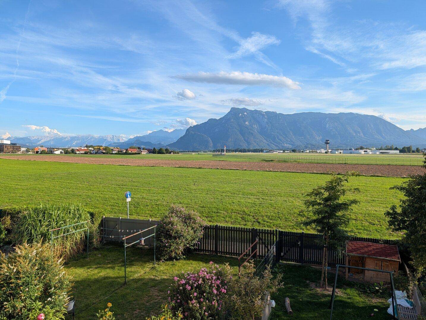 Weitläufiger Garten mit Rasenfläche, Zaun und beeindruckendem Bergblick.