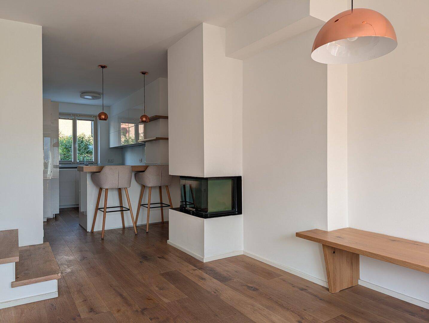 Moderner Wohnbereich mit Kamin, Holzboden und offener Verbindung zur Küche.