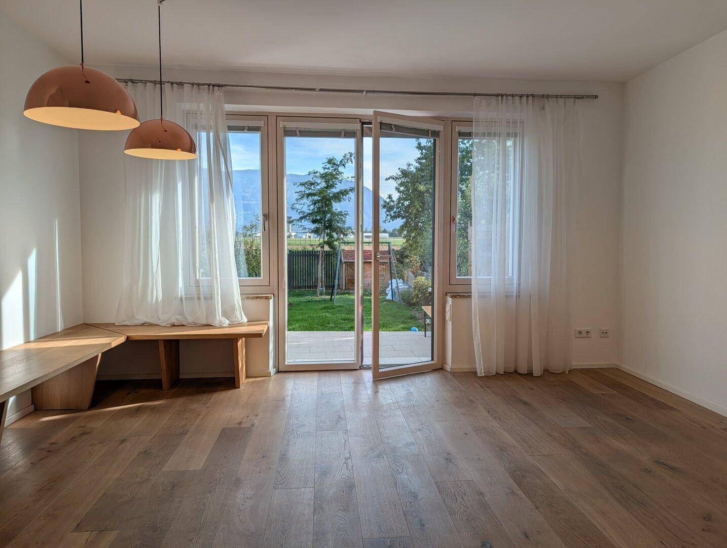 Helles Wohnzimmer mit Holzboden, großen Fenstern und direktem Zugang zum Garten.
