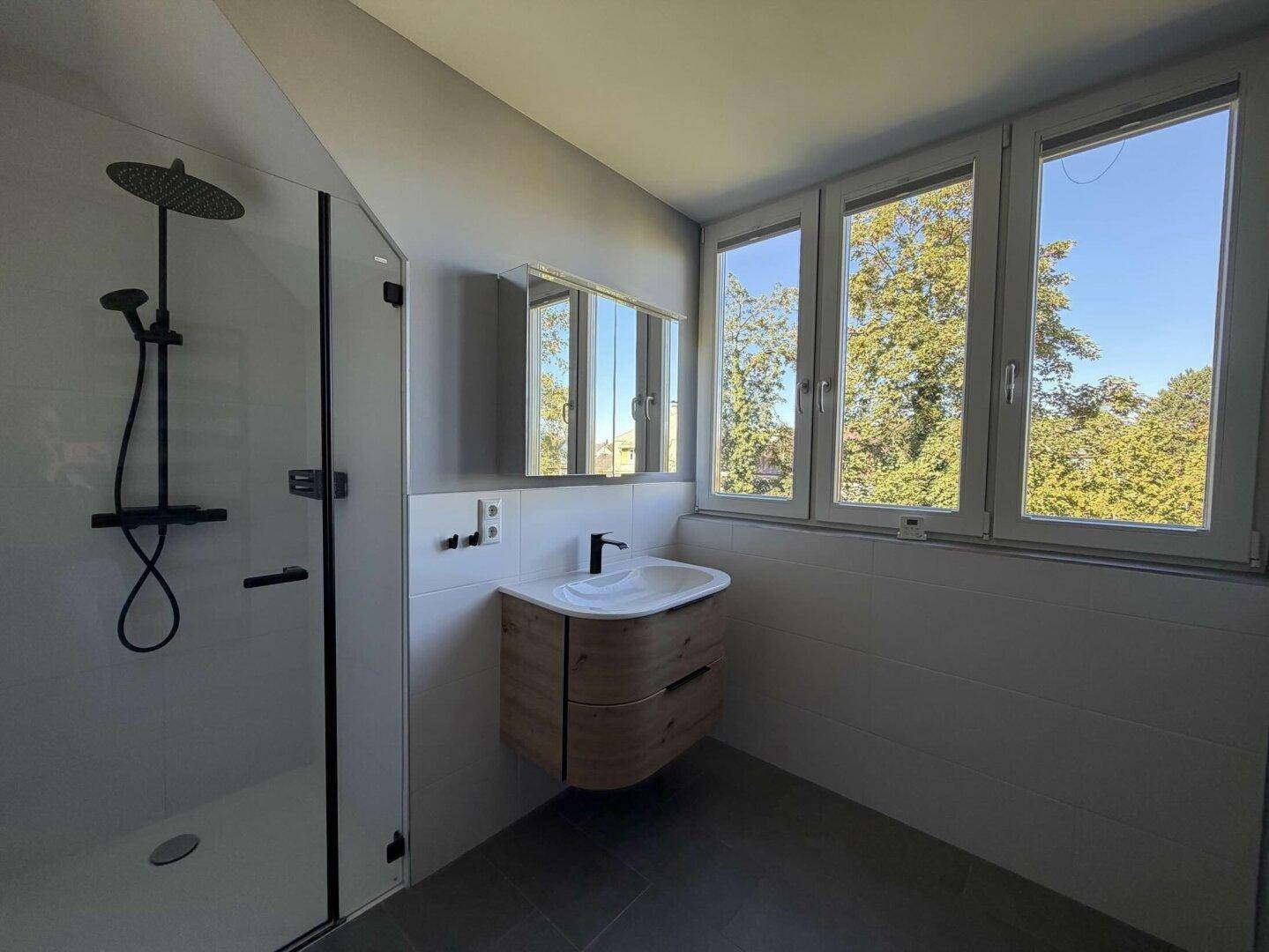 Modernes Badezimmer mit ebenerdiger Dusche, Holzwaschtisch und großen Fenstern.