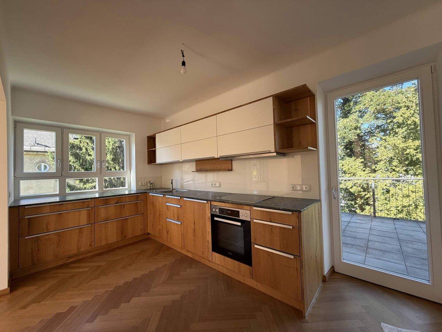 Moderne Küche mit Holzfronten, weißen Oberschränken und Zugang zu einem Balkon.