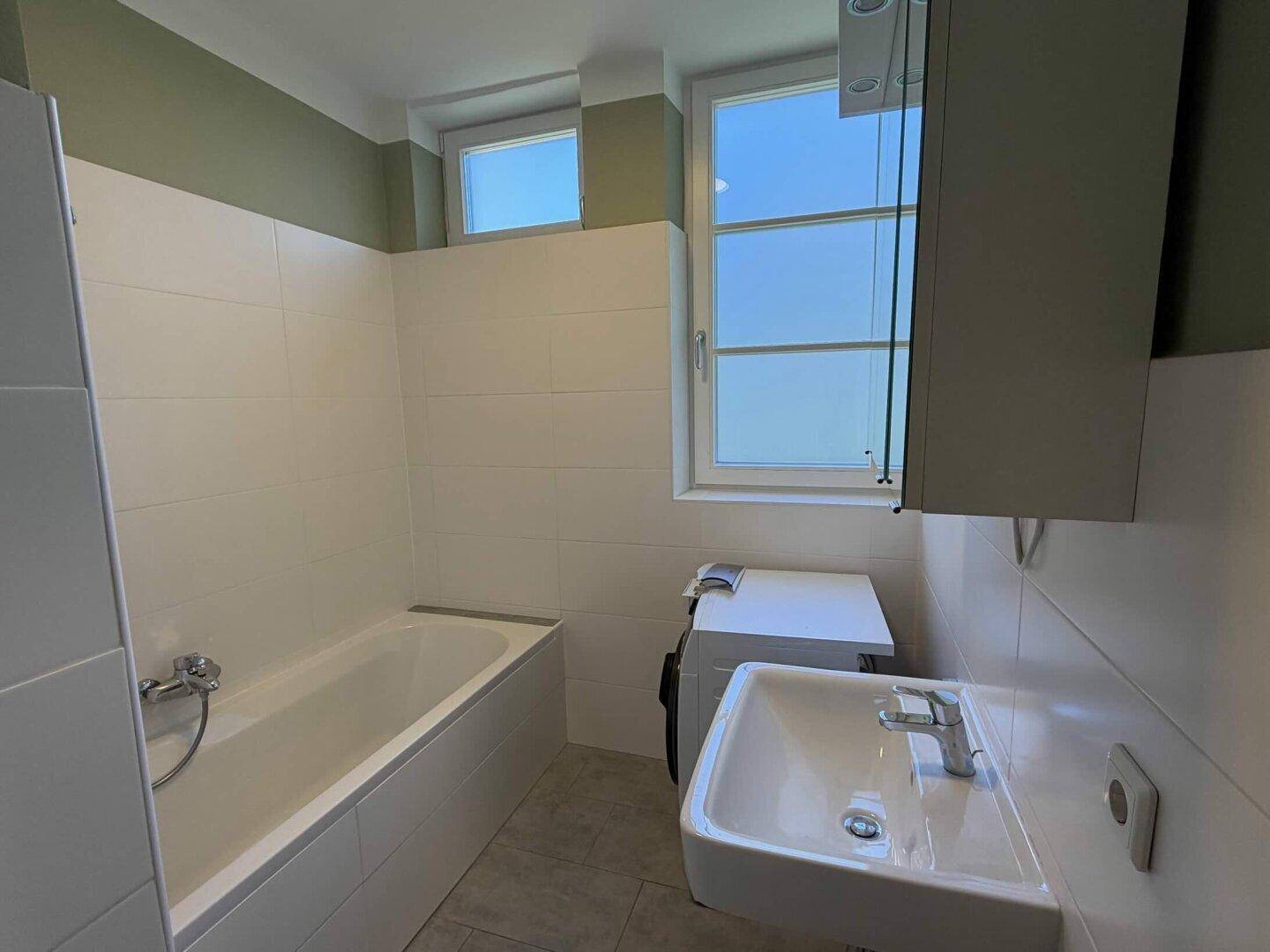 Helles Badezimmer mit Badewanne, Waschbecken und Fenster.
