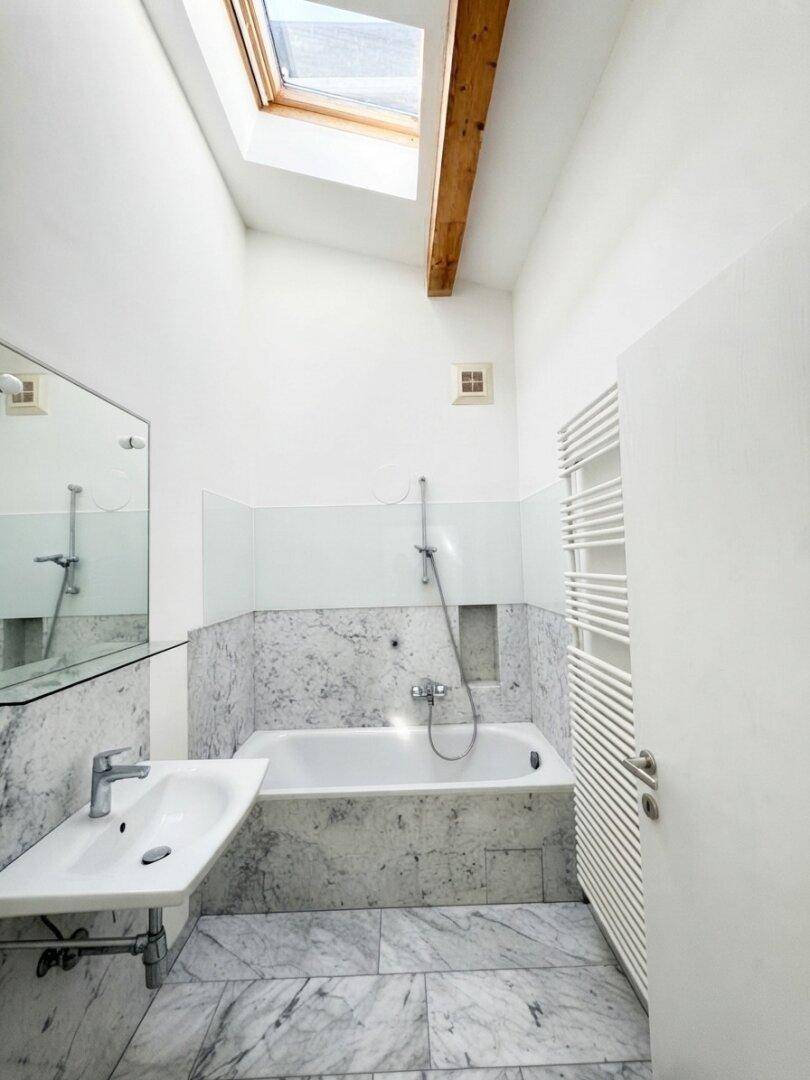 Modernes Badezimmer mit Marmorfliesen, Badewanne, Einzelwaschbecken, beheiztem Handtuchhalter und Dachfenster.