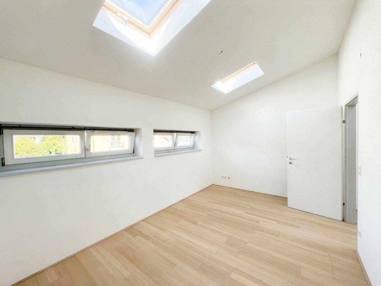 Helles Schlafzimmer mit Holzboden, zwei Fenstern und zwei Dachfenstern für viel natürliches Licht.