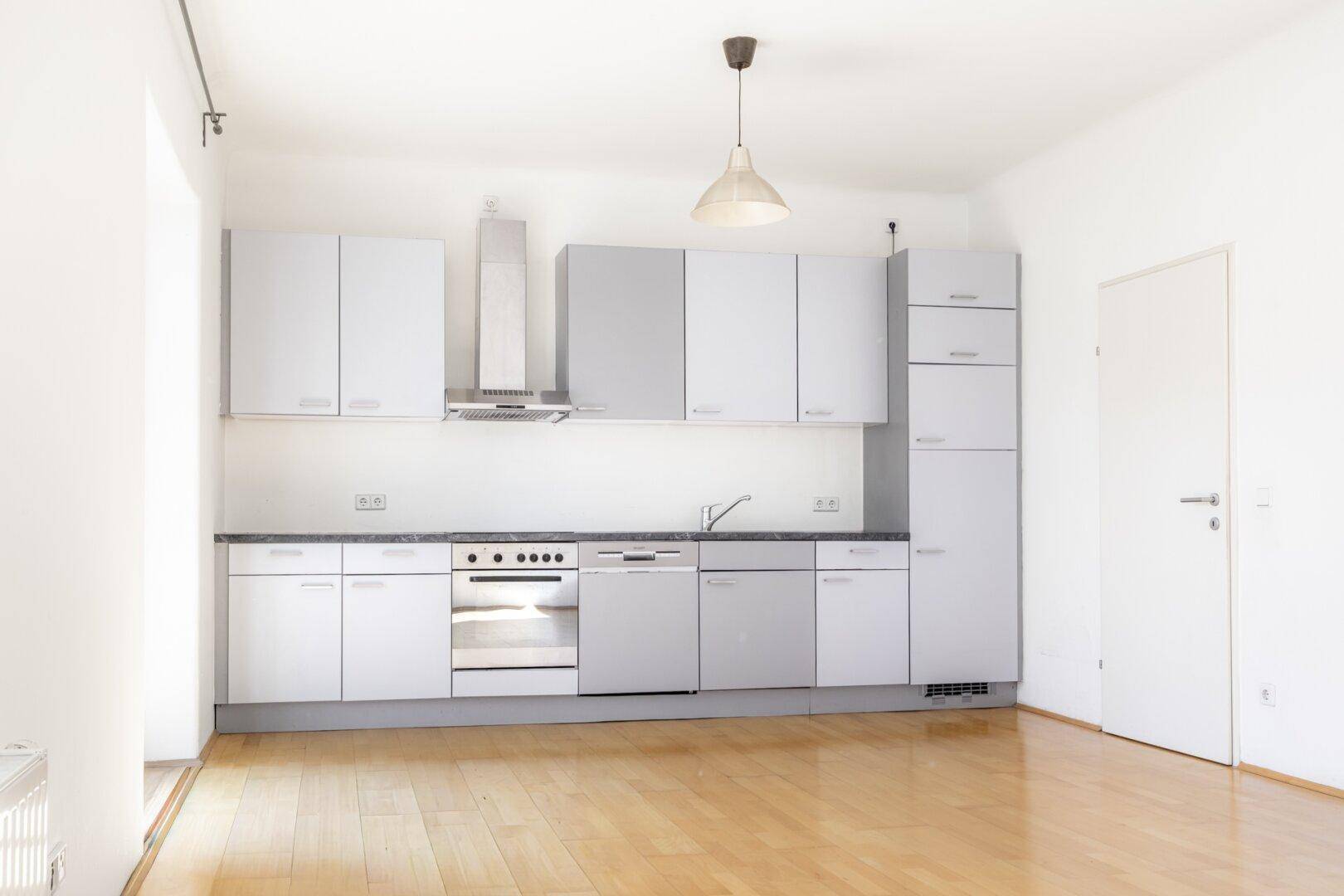 Moderne Einbauküche in Grau und Weiß mit integrierten Geräten und Parkettboden.