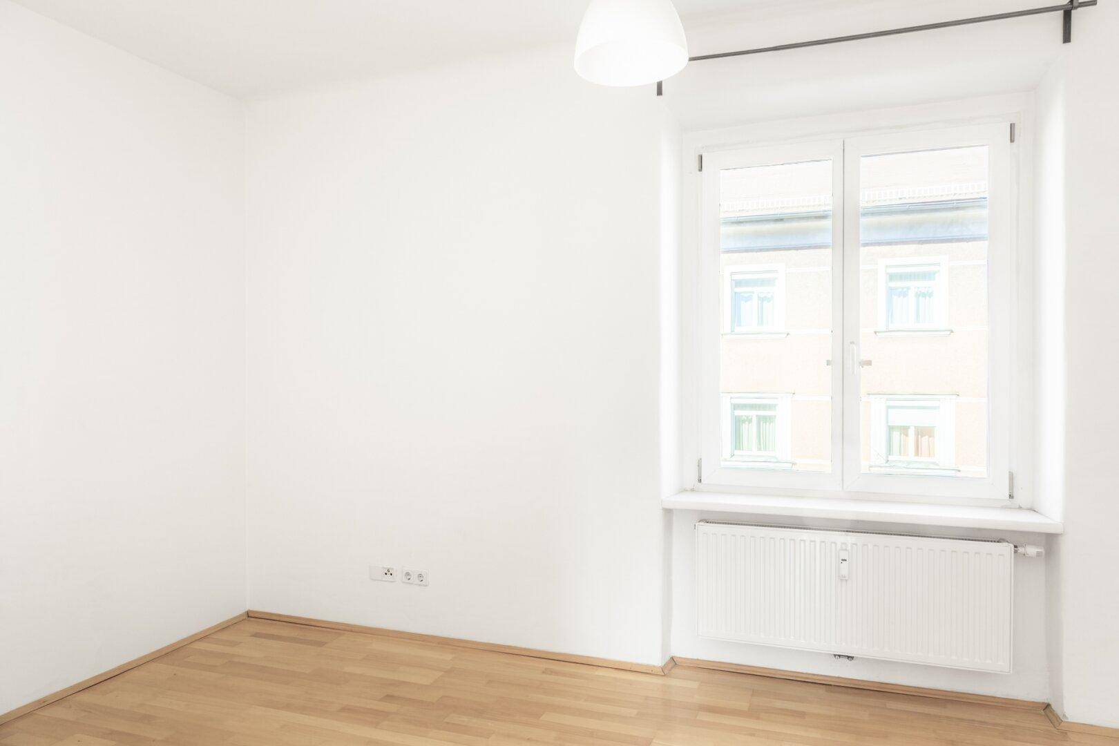 Helles Zimmer mit Parkettboden, großem Fenster und Heizkörper, ideal als Schlafzimmer.