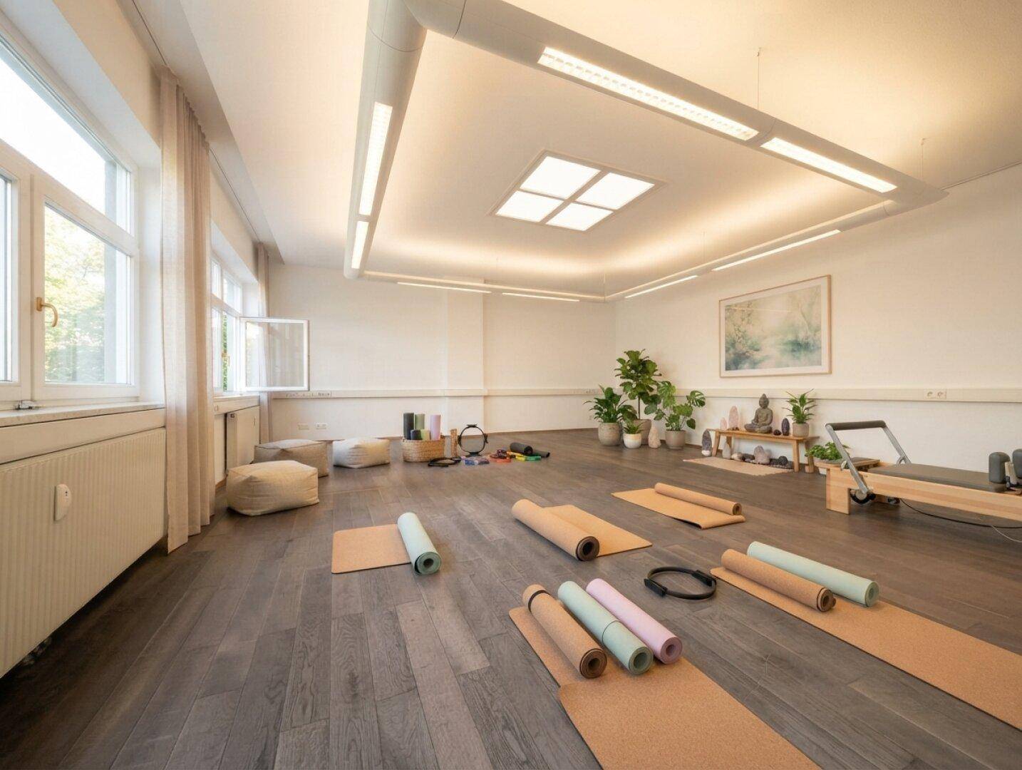 Heller Raum, eingerichtet als Yogastudio mit Matten, Kissen und vielen Pflanzen, ideal für Kurse.