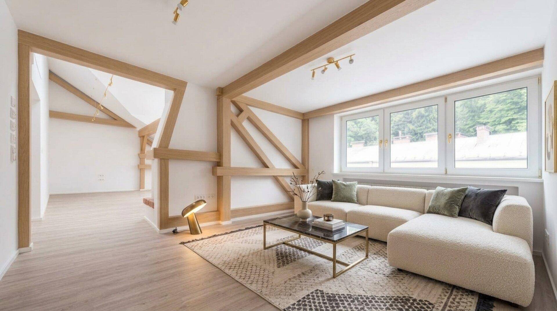Helles Wohnzimmer mit modernen Holzbalken, großen Fenstern und Blick ins Grüne, ausgestattet mit einem bequemen Sofa.