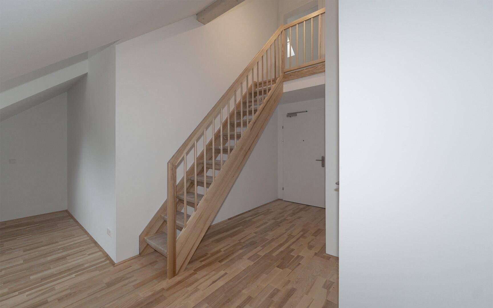 Heller Flur mit Holztreppe und Parkettboden, der zu weiteren Räumen führt.