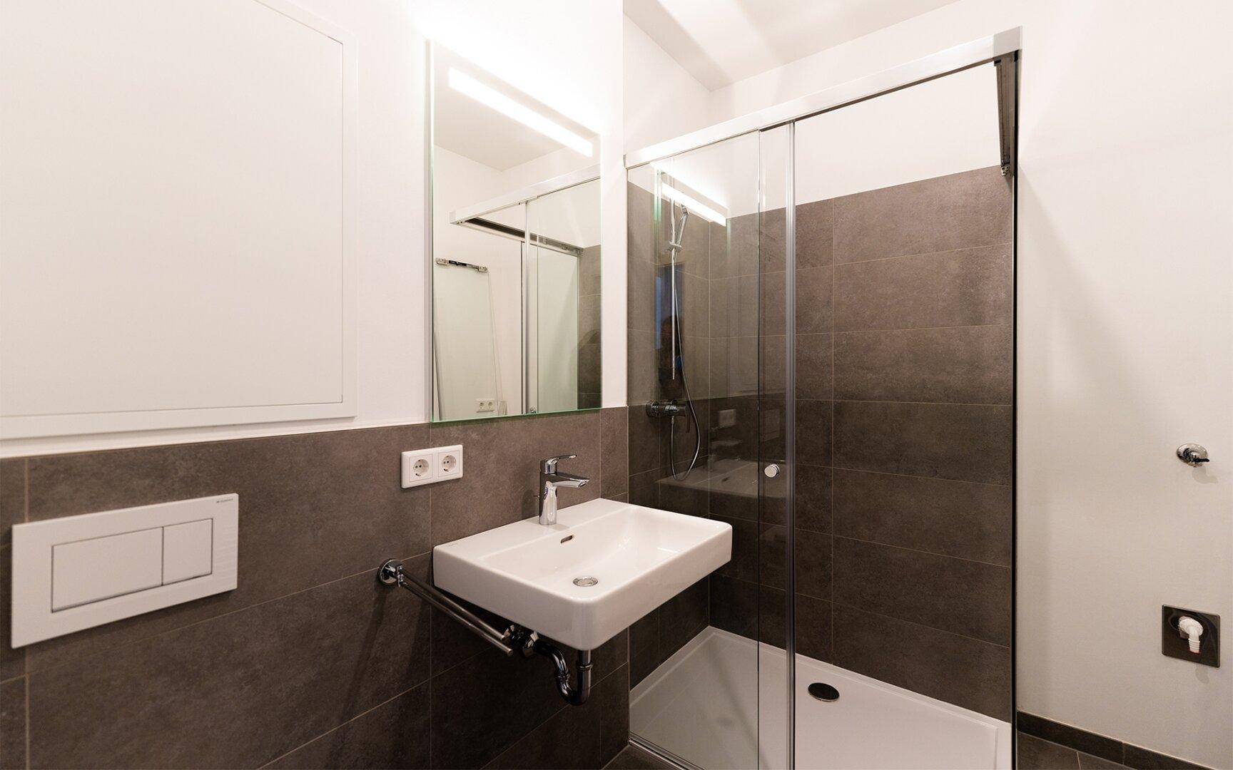 Modernes Badezimmer mit ebenerdiger Dusche, Einzelwaschbecken und dunklen Fliesen.