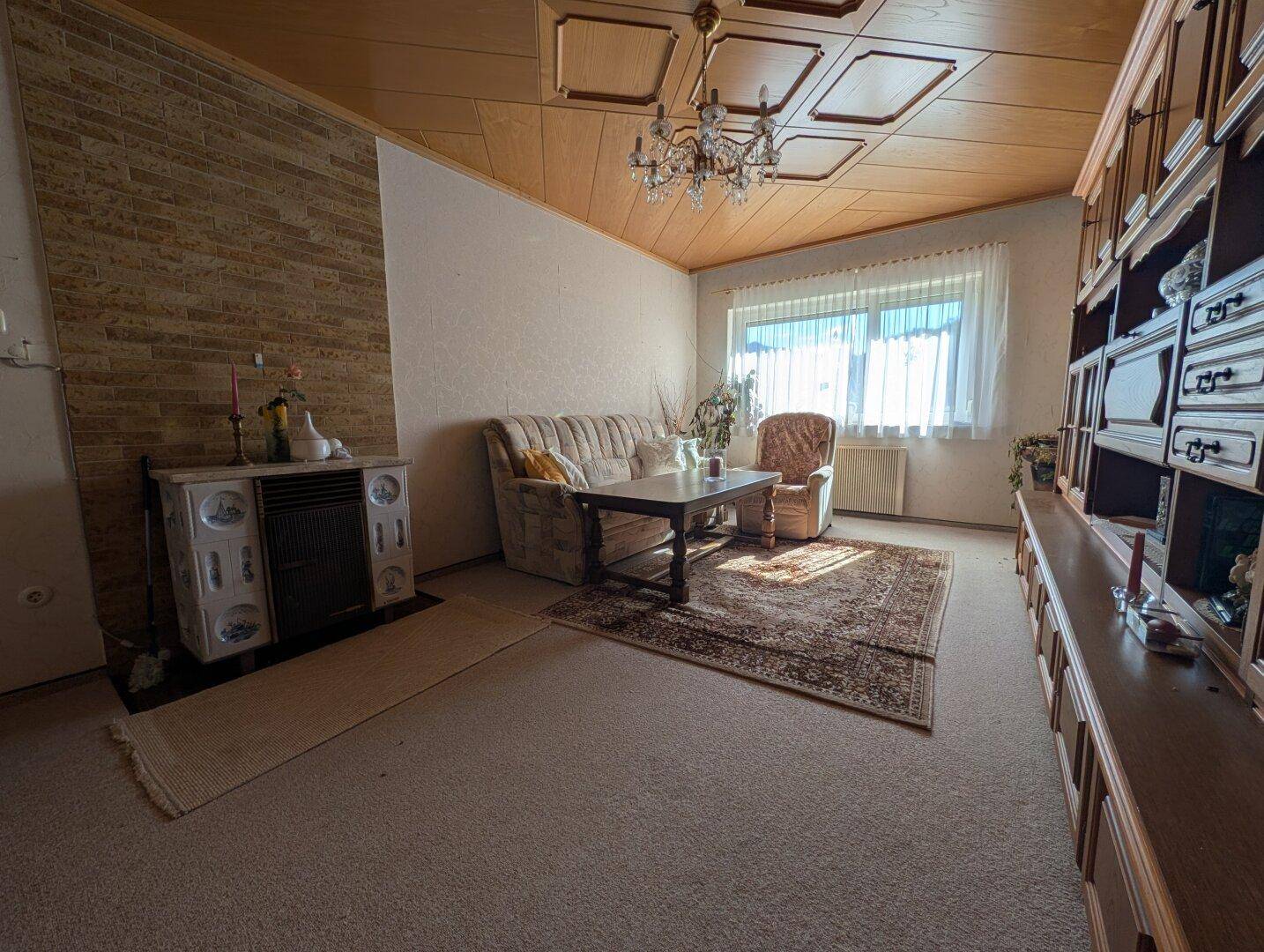 Gemütliches Wohnzimmer mit traditionellem Kachelofen, Teppichboden und Holzdecke.