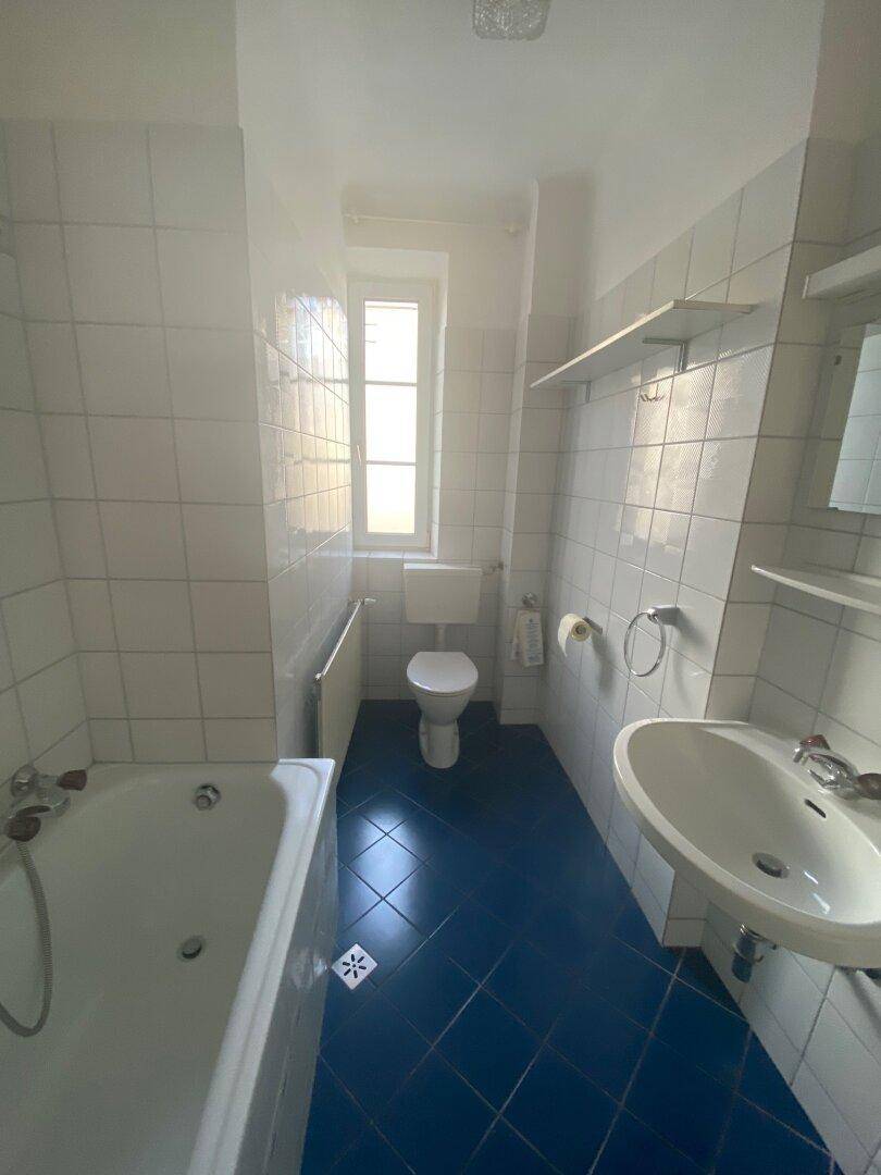 Badezimmer mit blauen Fliesen, Badewanne, Waschbecken und Fenster für Tageslicht.