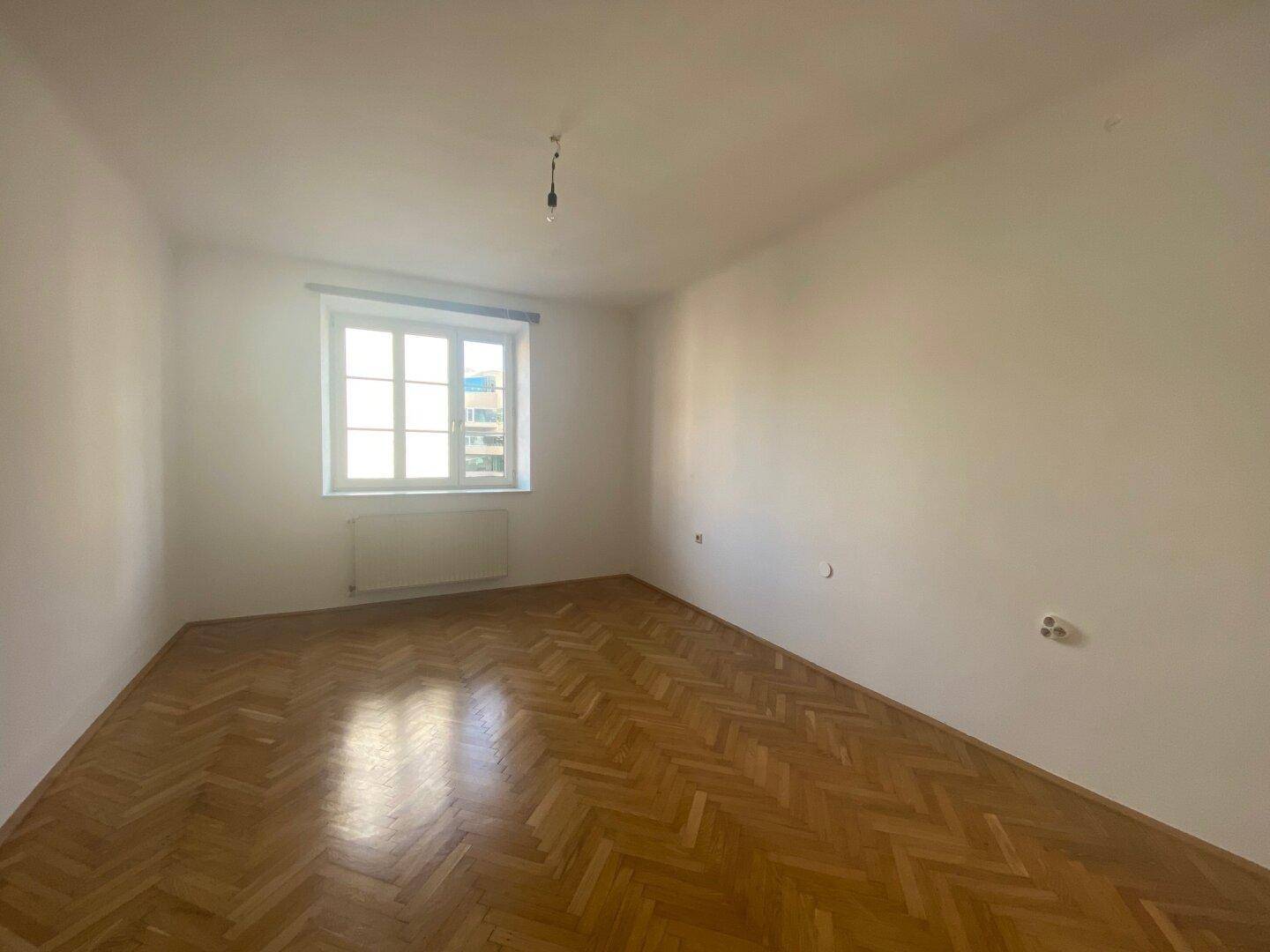 Leerer Raum mit Fischgrätparkett und einem Fenster, bereit zur individuellen Gestaltung.