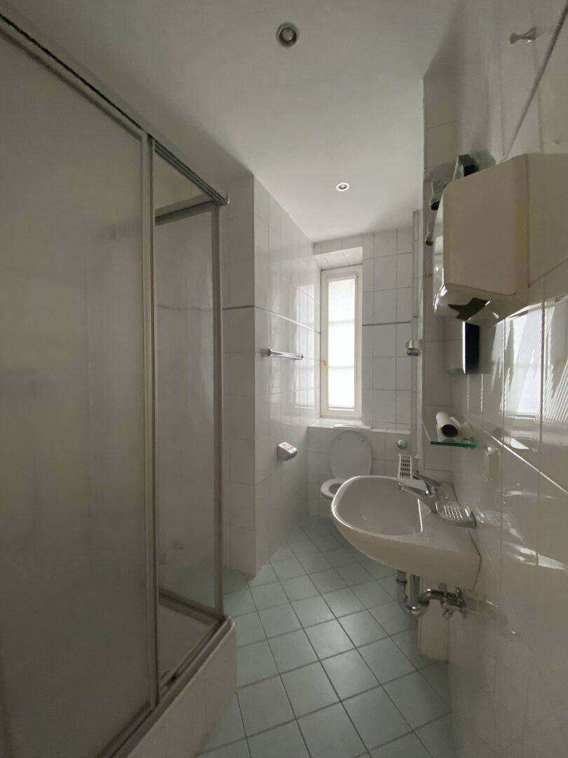 Gefliestes Badezimmer mit Duschkabine, Waschbecken und Fenster.