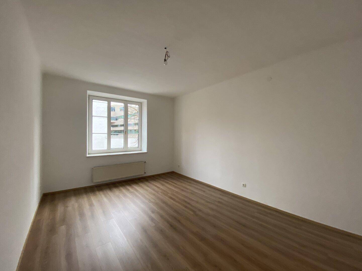 Helles Schlafzimmer mit Laminatboden und einem großen Fenster.