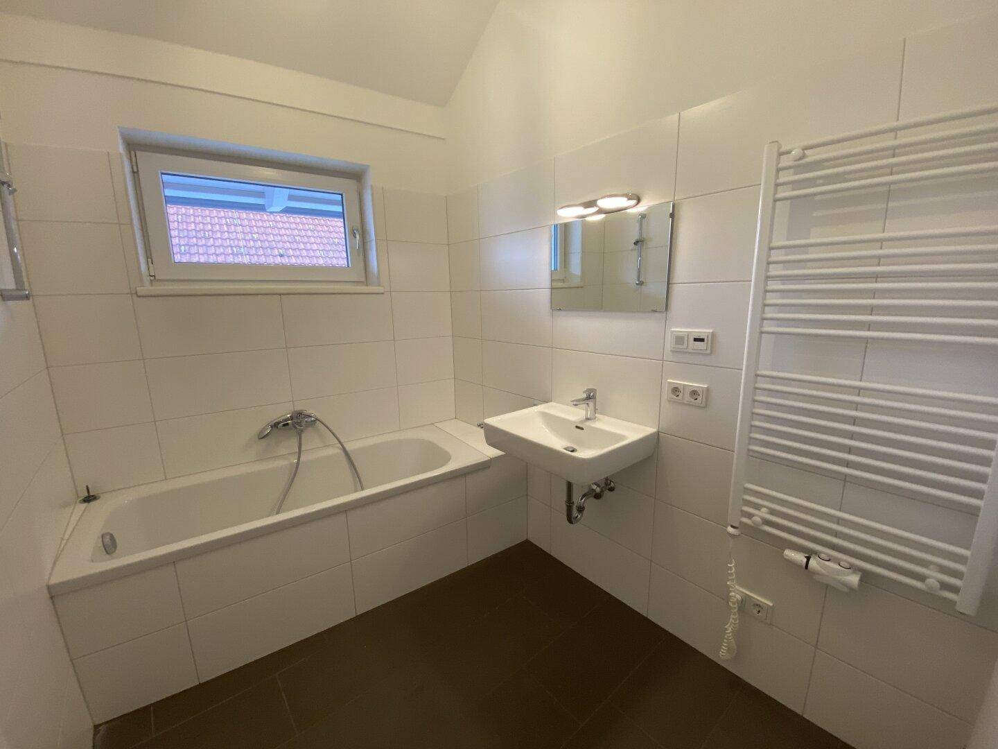 Modernes Badezimmer mit Badewanne, Waschbecken, beheiztem Handtuchhalter und Fenster.