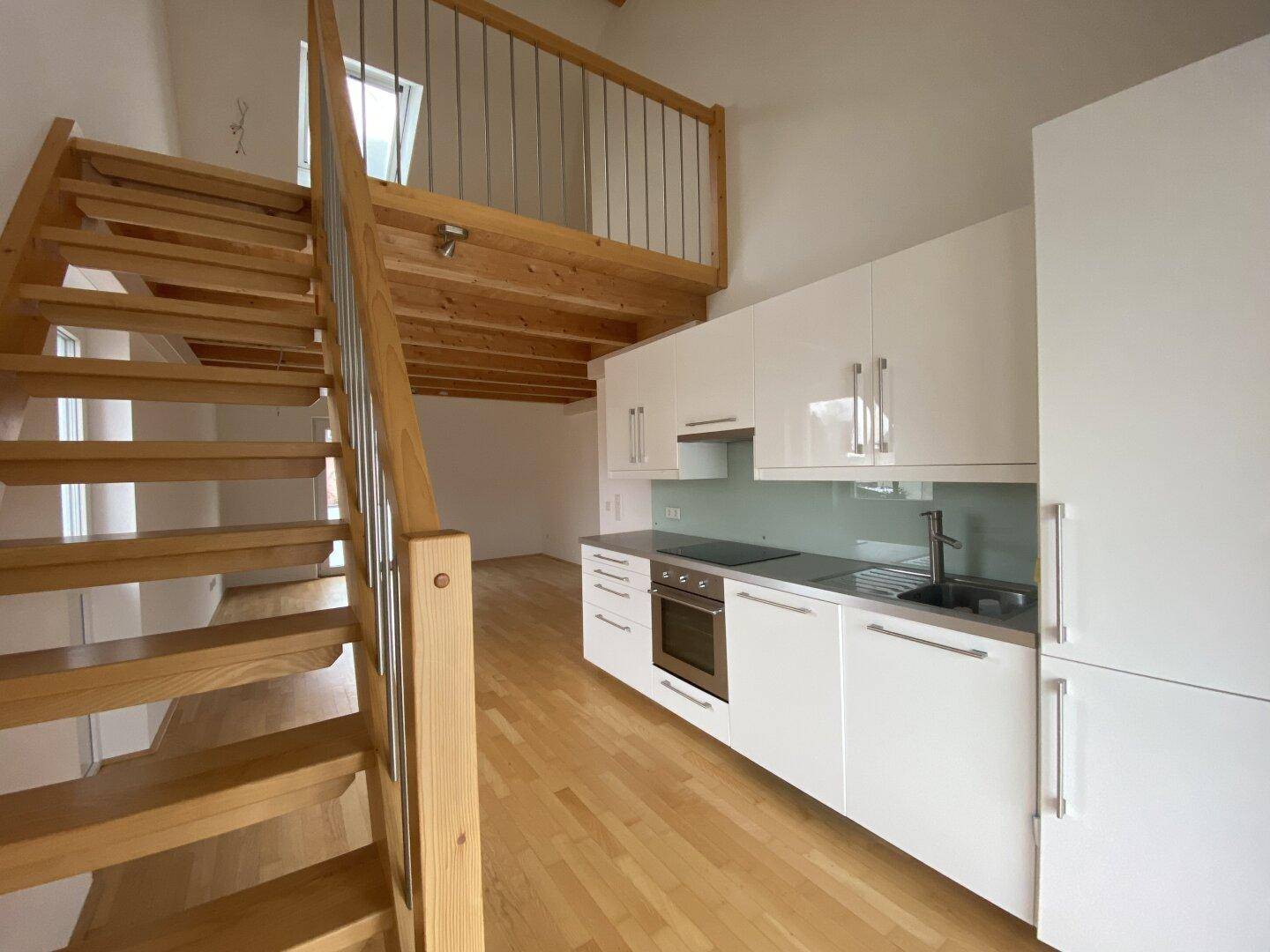 Helle Einbauküche mit weißen Schränken und Holztreppe, die zu einem offenen Galeriebereich führt.