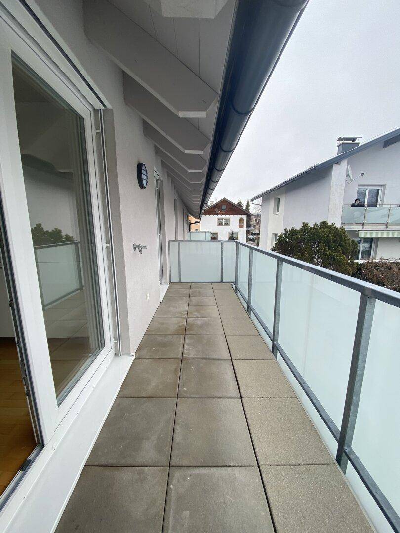 Langer Balkon mit Fliesenboden und moderner Glasbrüstung, bietet Blick auf die Umgebung.