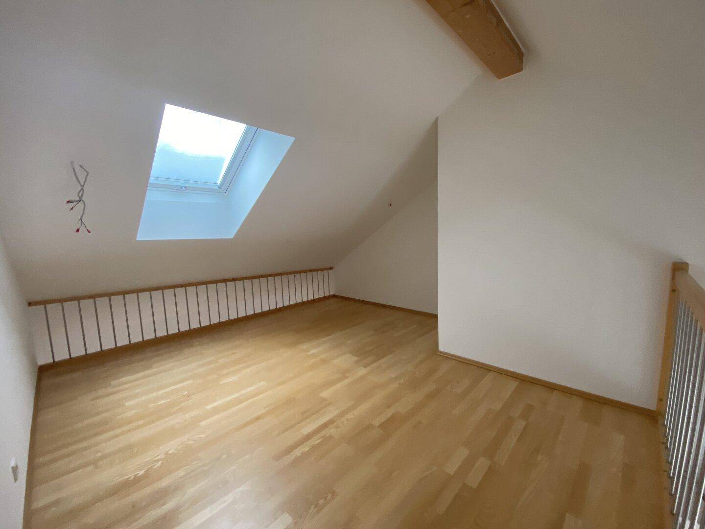 Heller Dachgeschossraum mit Holzboden und großem Dachfenster, ideal als Schlaf- oder Arbeitsbereich.