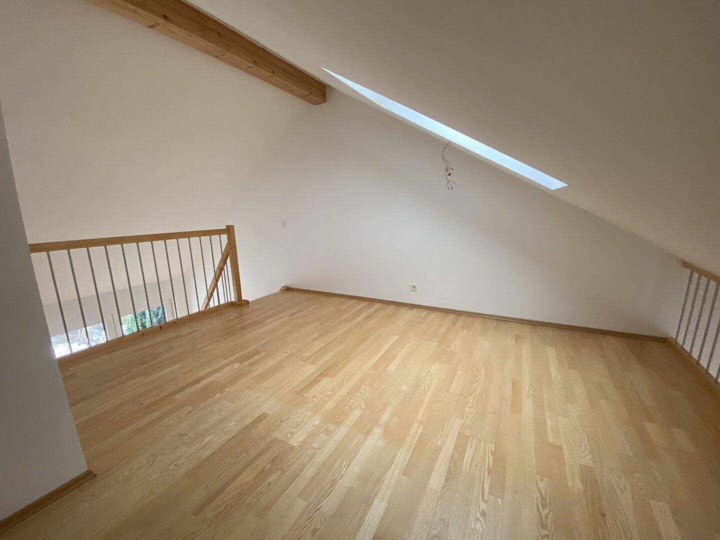 Offener Galeriebereich mit Holzboden, Dachschräge und einem Dachfenster, das viel Licht spendet.