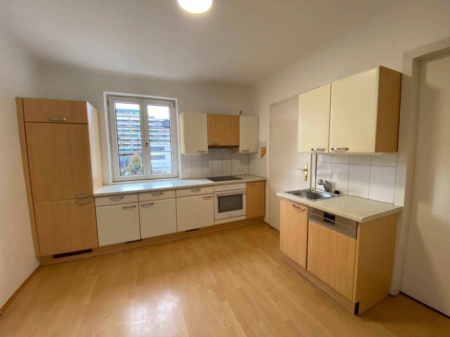 Helle Einbauküche mit Holzfronten, integrierten Geräten und einem Fenster für Tageslicht.