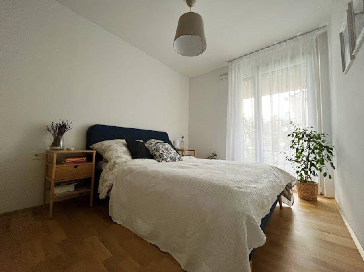 Helles Schlafzimmer mit Holzboden, großem Fenster und einem bequemen Doppelbett.